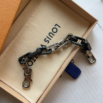 A Louis Vuitton chain accessory with black and silver links, displayed on its beige branded dust bag inside an open Louis Vuitton box.