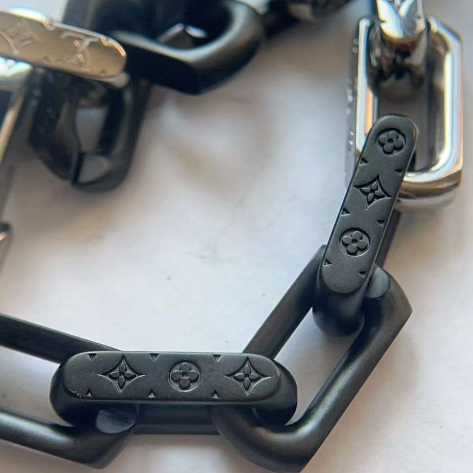 Close-up of a chunky chain link bracelet featuring matte black links with embossed Louis Vuitton monogram motifs and polished silver-tone links.