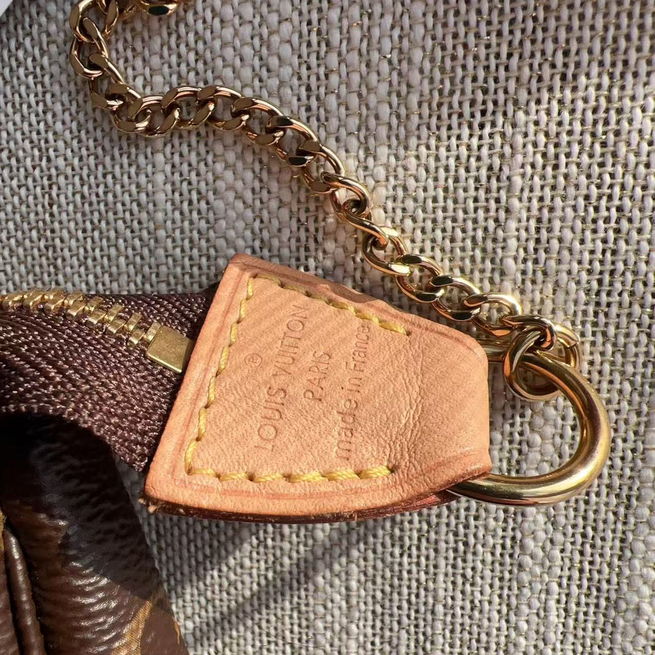 Close-up of a Louis Vuitton bag tag with chain on a textured surface