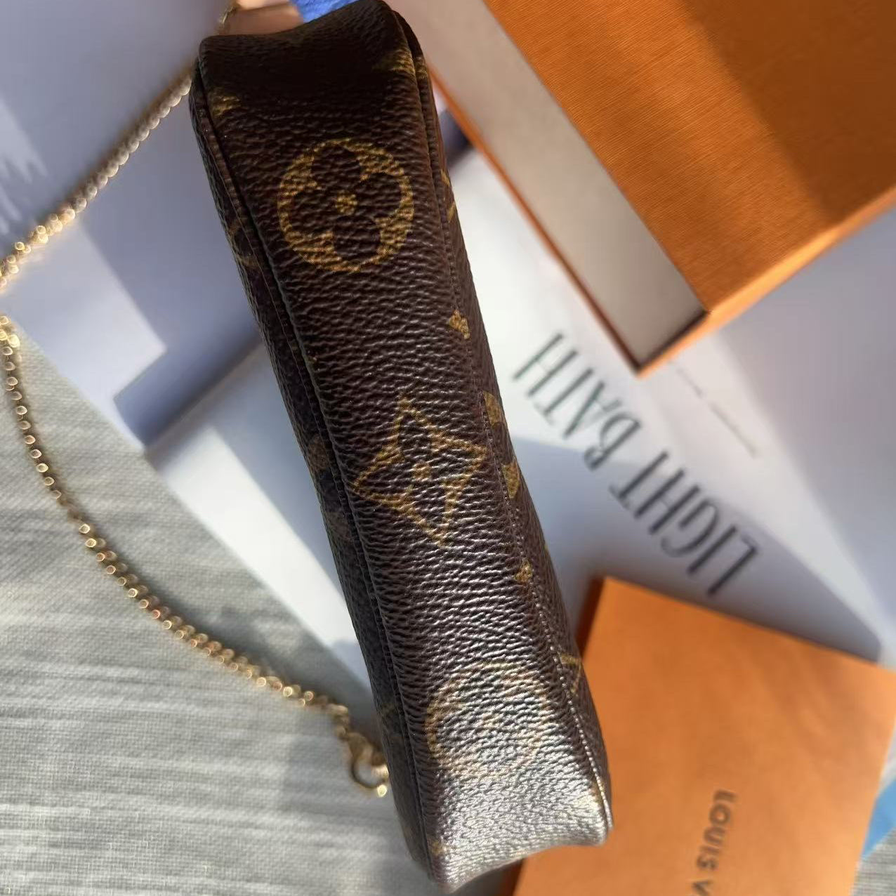 Louis Vuitton lip balm case with chain on a light gray surface