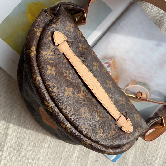 A Louis Vuitton monogrammed half-moon shoulder bag in brown coated canvas with tan leather trim, shown resting on a light-colored textured surface with printed papers underneath.