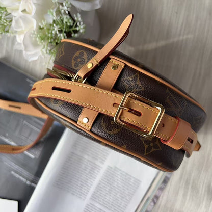 Louis Vuitton monogram canvas shoulder bag with tan leather straps and gold-tone hardware, photographed on a light wood surface with a magazine and white flowers as props.