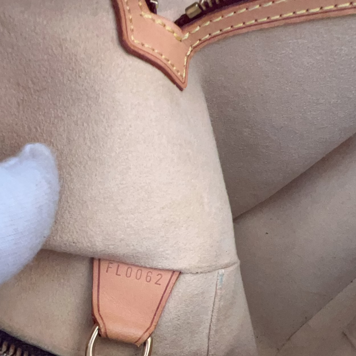 Close-up of a beige handbag with leather accents and a visible brand tag.