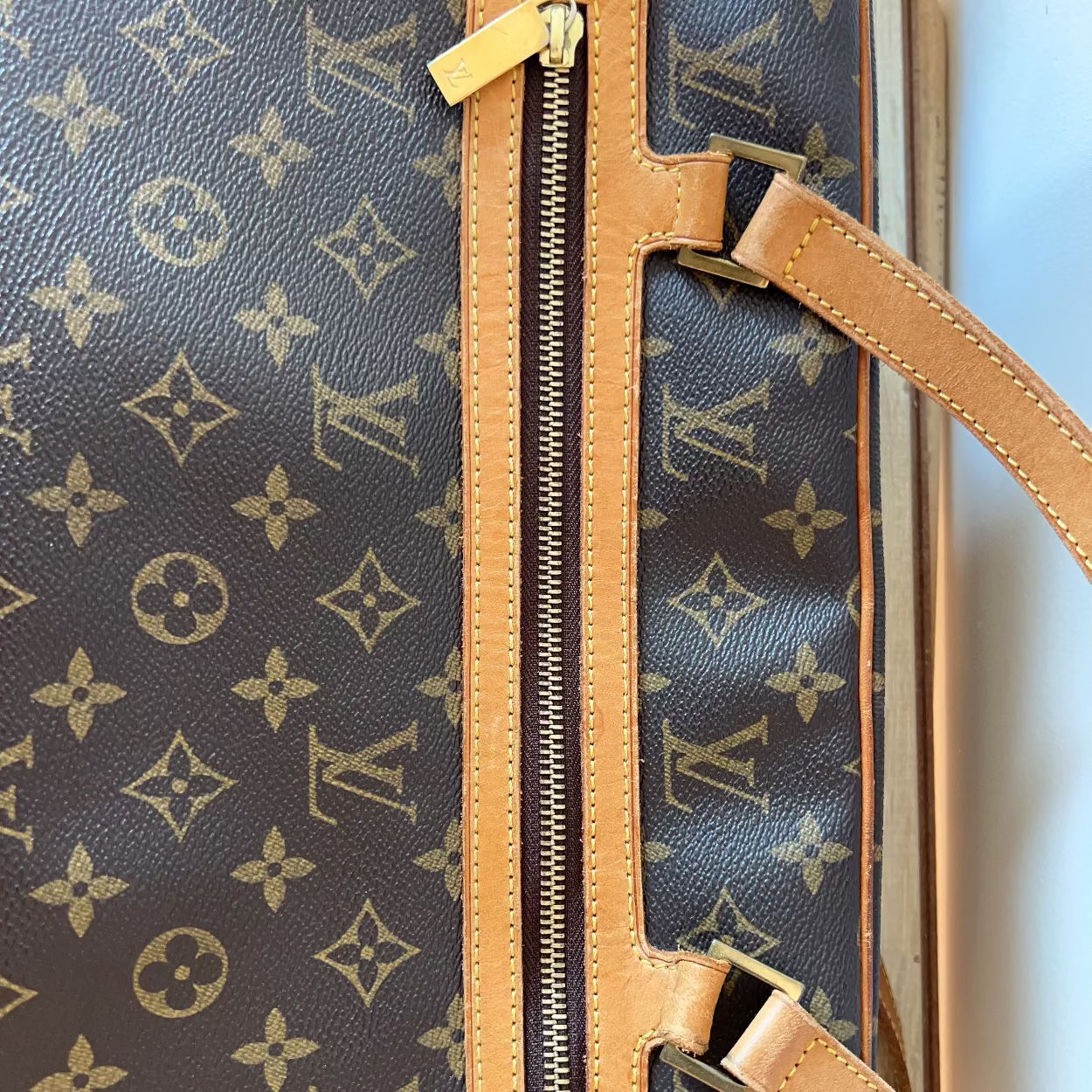 Close-up of a Louis Vuitton handbag with monogram pattern and tan leather handle.