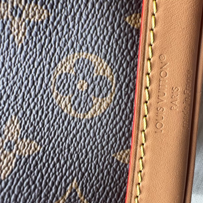 Close-up of a Louis Vuitton monogram canvas item with tan leather trim and yellow stitching, showing embossed 'LOUIS VUITTON S.A.
