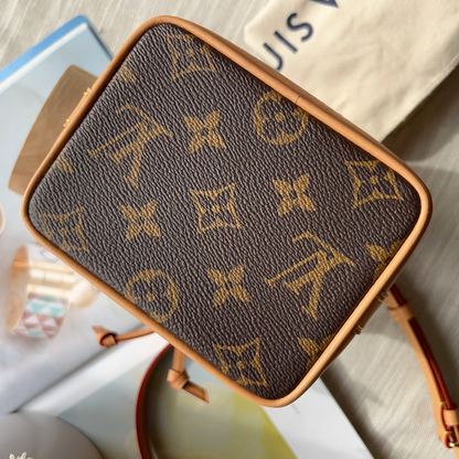 A Louis Vuitton monogram crossbody bag in brown coated canvas with tan leather trim, shown resting on a light-colored surface with a dust bag and magazine visible in the background.