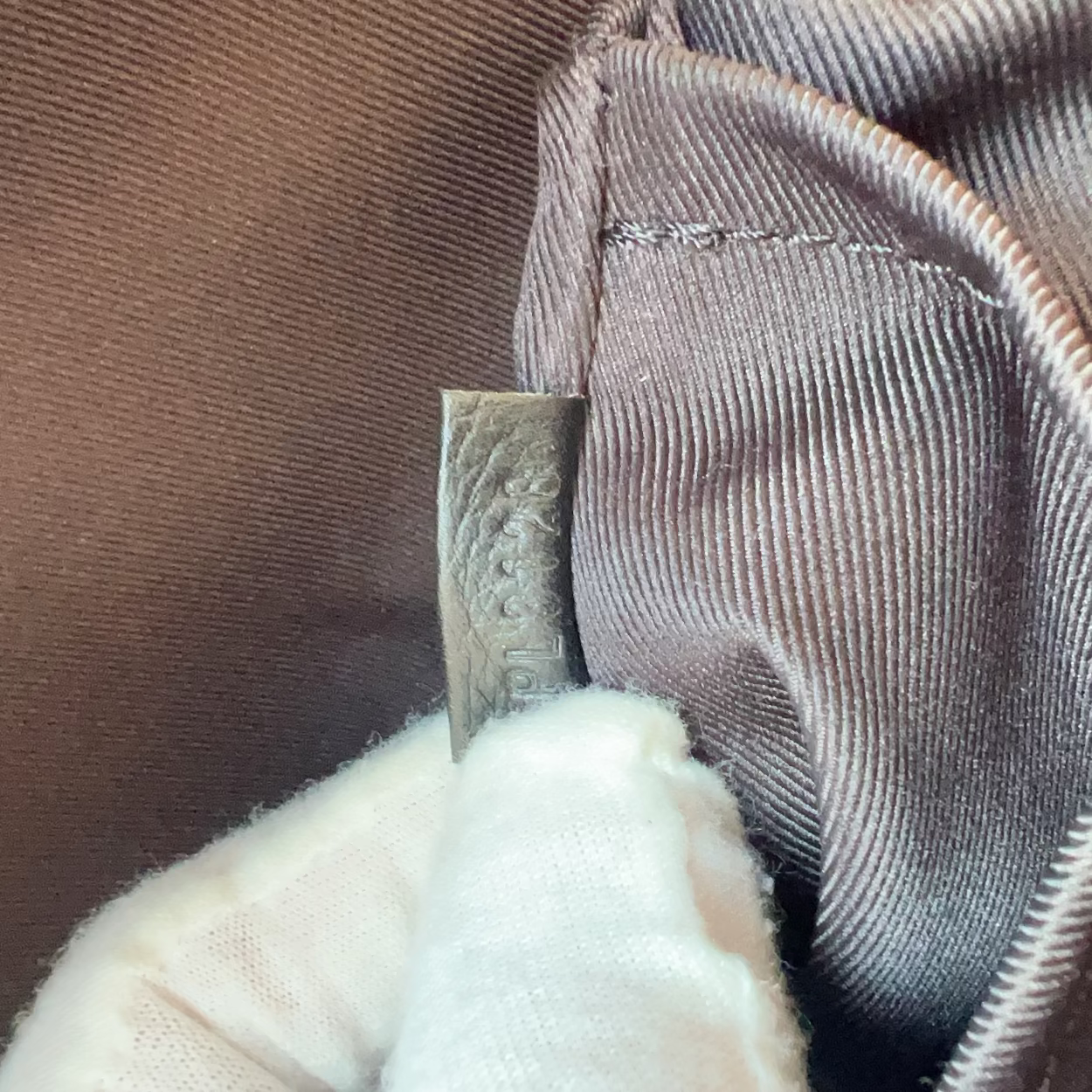 Close-up of a textured fabric with a metal tag and white cloth underneath.