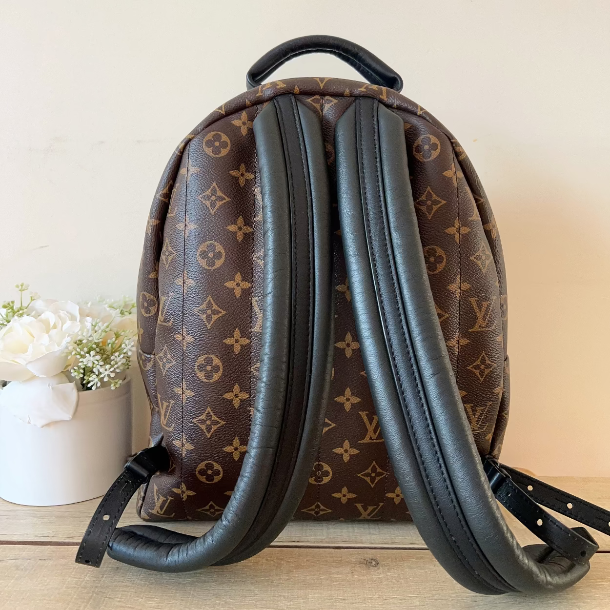 Brown monogram backpack with black straps on a light wooden surface.