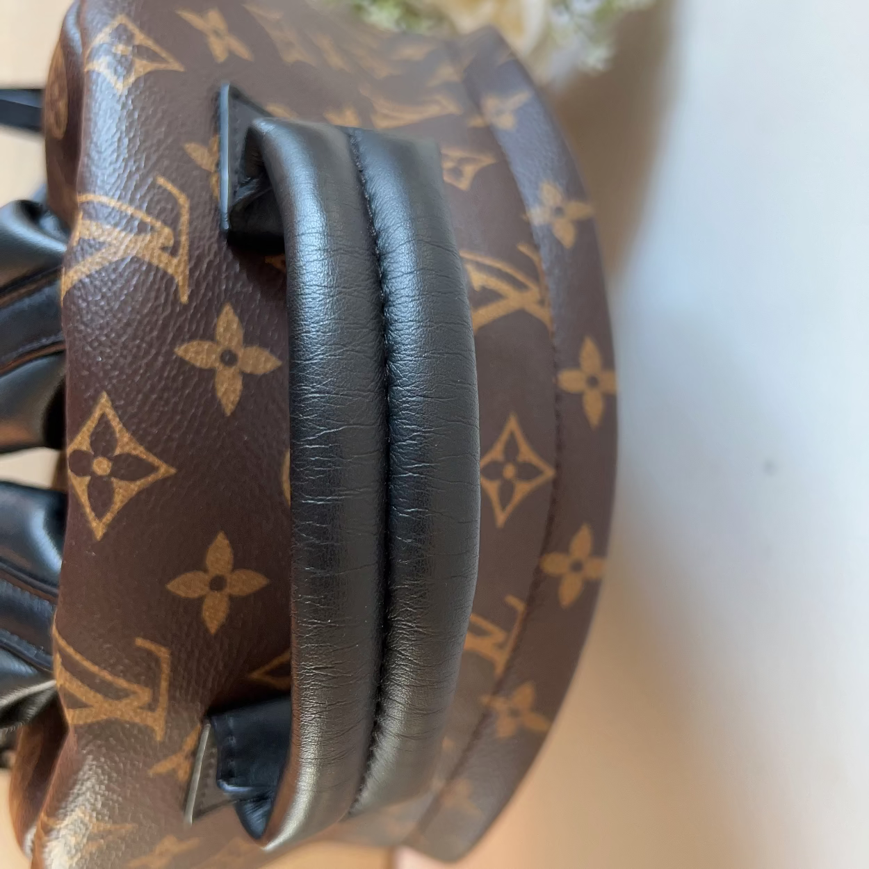 Louis Vuitton-patterned headphones on a white surface with flowers in the background