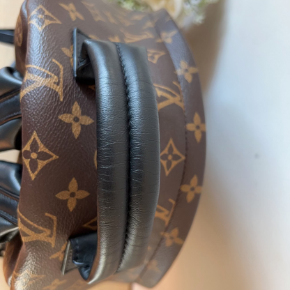 Louis Vuitton-patterned headphones on a white surface with flowers in the background