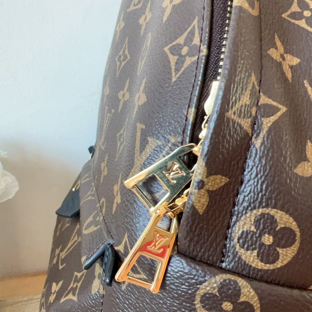 Close-up of a Louis Vuitton monogram handbag with a gold lock on a light background
