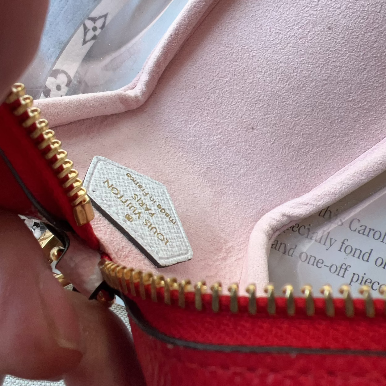 Close-up of a red handbag with gold zipper and visible brand label.