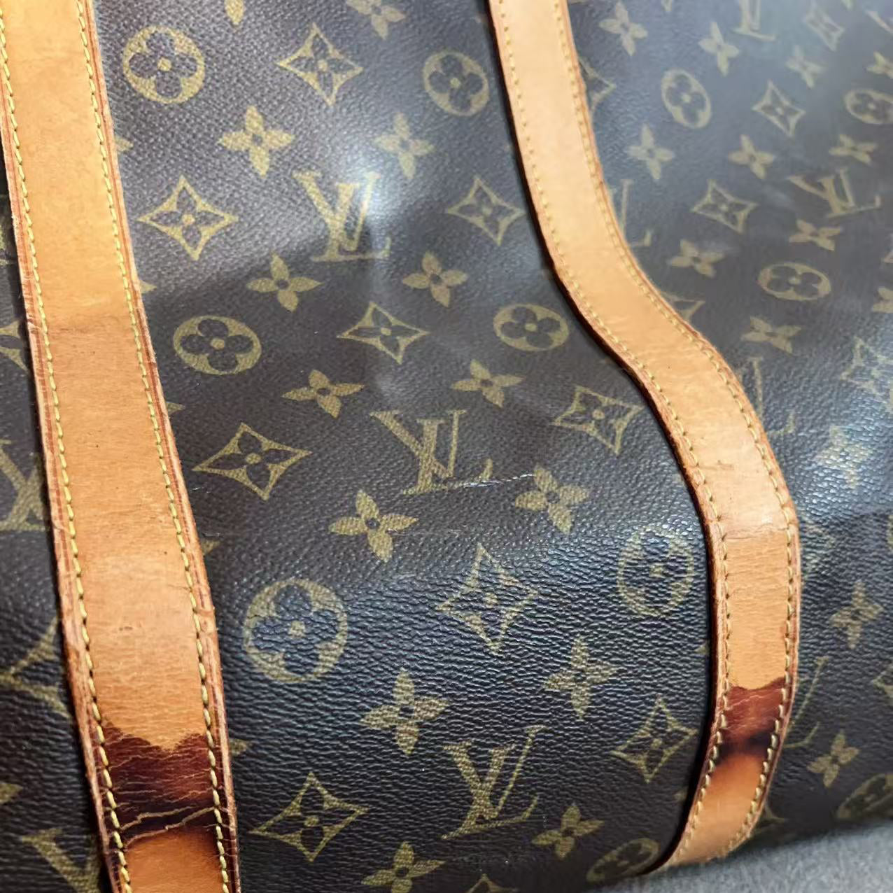 Close-up of a Louis Vuitton monogram duffle bag showing the dark brown coated canvas with tan monogram print and tan leather trim straps.