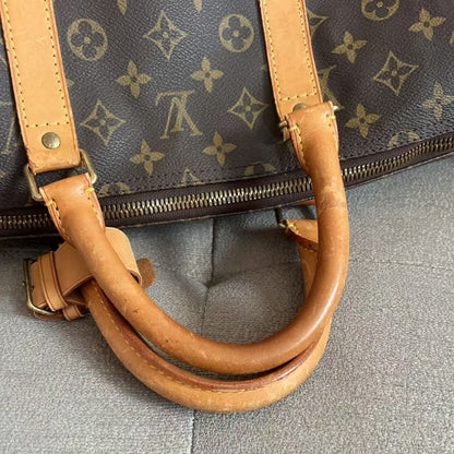 Close-up of a Louis Vuitton monogram duffel bag with tan leather handles and a gold-tone zipper, resting on a gray fabric surface.