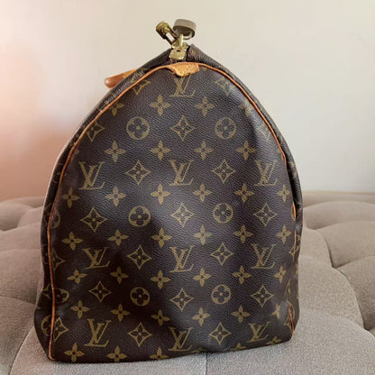 A Louis Vuitton monogram canvas dust bag or small bag with a rounded top and gold-tone zipper, resting on a gray tufted surface against a plain light wall.