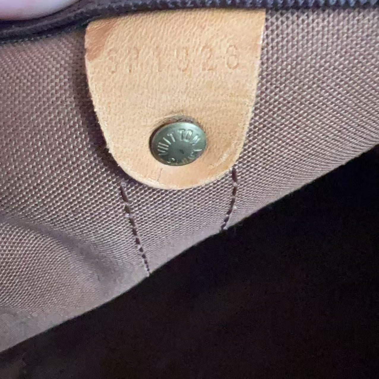 Close-up of a brown canvas and dark brown leather bag interior showing a tan leather tab with a brass snap and stamped numbers, held by a finger.