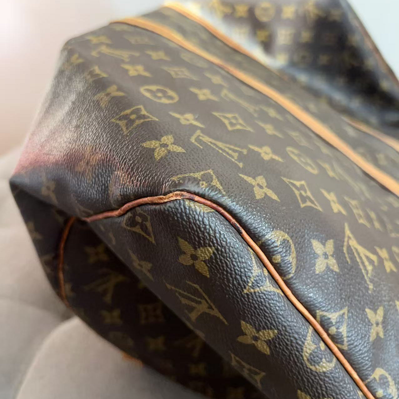 Close-up of a Louis Vuitton monogram canvas bag in dark brown with tan monogram print and light tan piping, resting on a light gray surface.