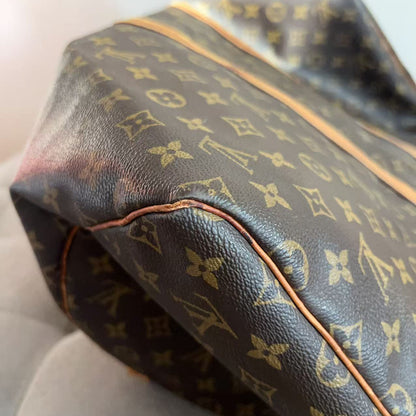 Close-up of a Louis Vuitton monogram canvas bag in dark brown with tan monogram print and light tan piping, resting on a light gray surface.