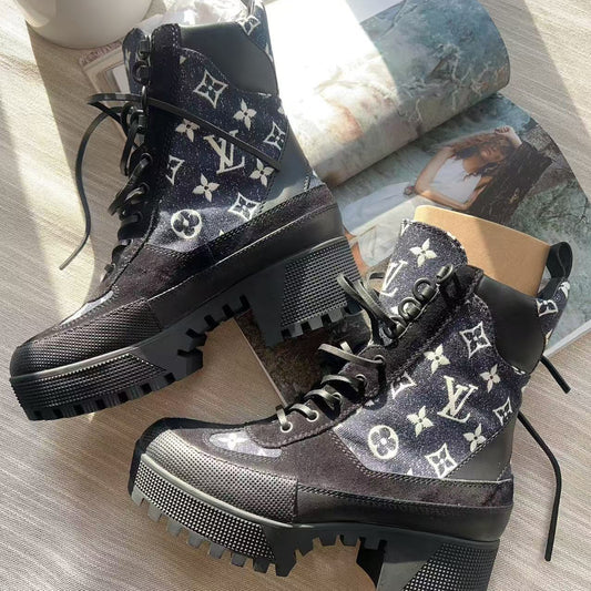 Black boots with white monogram pattern on a light wooden surface.