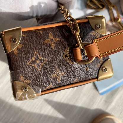 Close-up of a Louis Vuitton monogram canvas handbag with gold-tone hardware and a tan leather strap, held by a hand wearing a white glove.