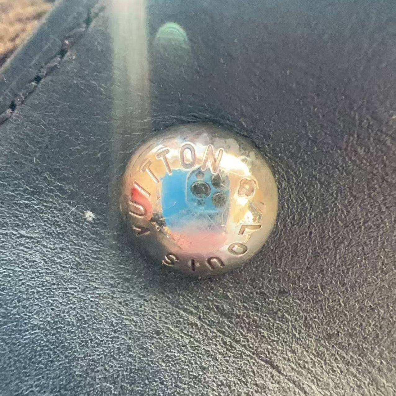 Gold button with 'Louis Vuitton' branding on a dark textured surface