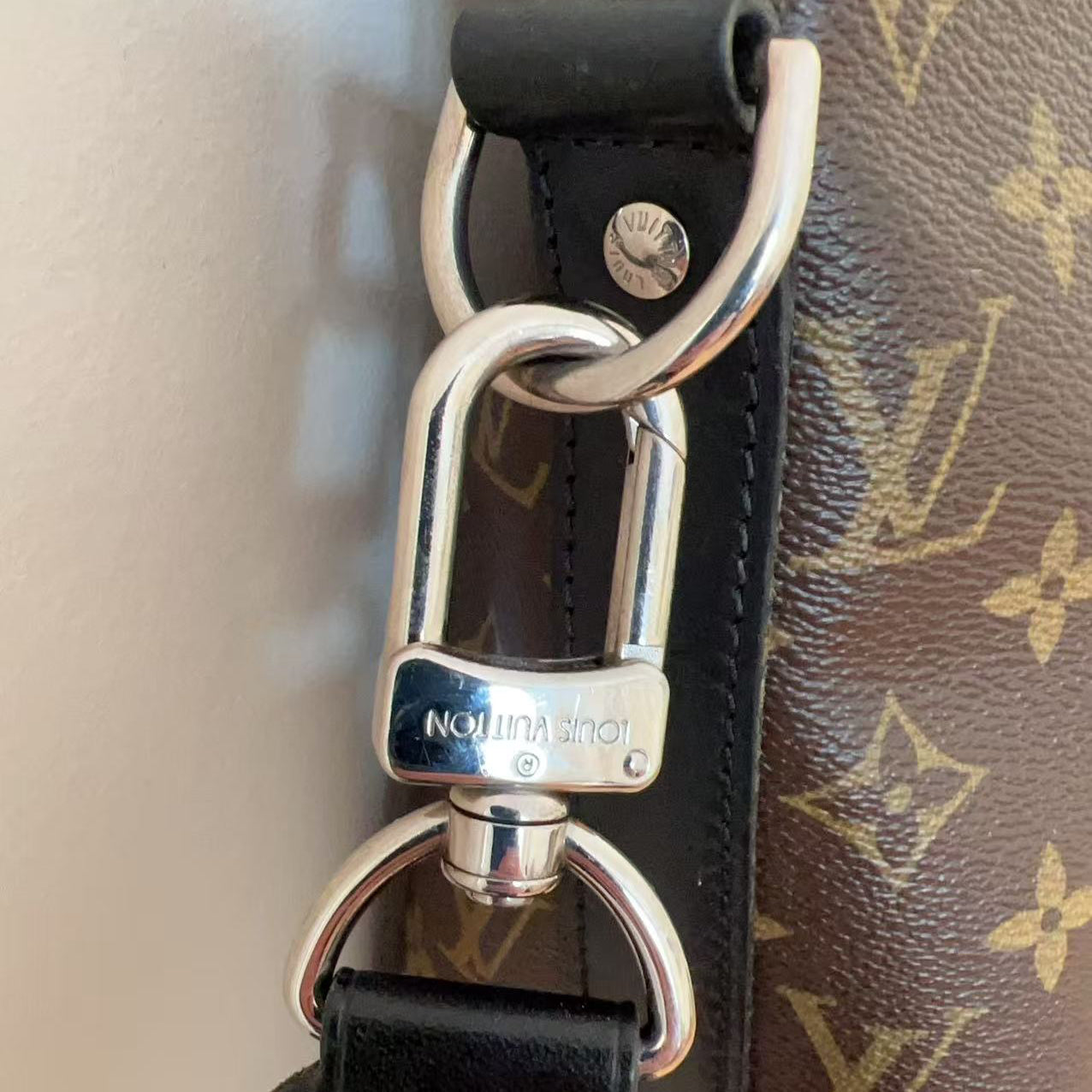 Close-up of a black leather strap with a silver clasp on a Louis Vuitton bag.