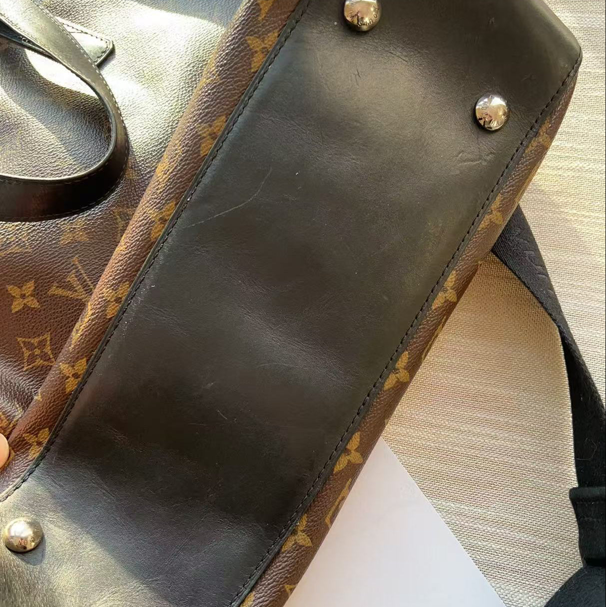 Brown leather bag with gold monogram pattern held by a hand on a light background