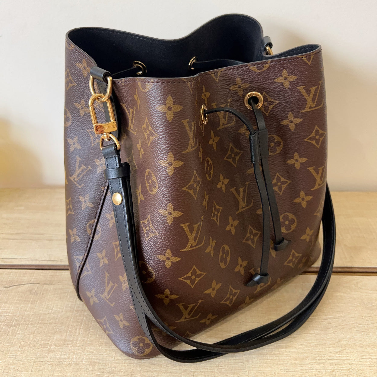 Brown leather handbag with monogram pattern on a light wooden surface.