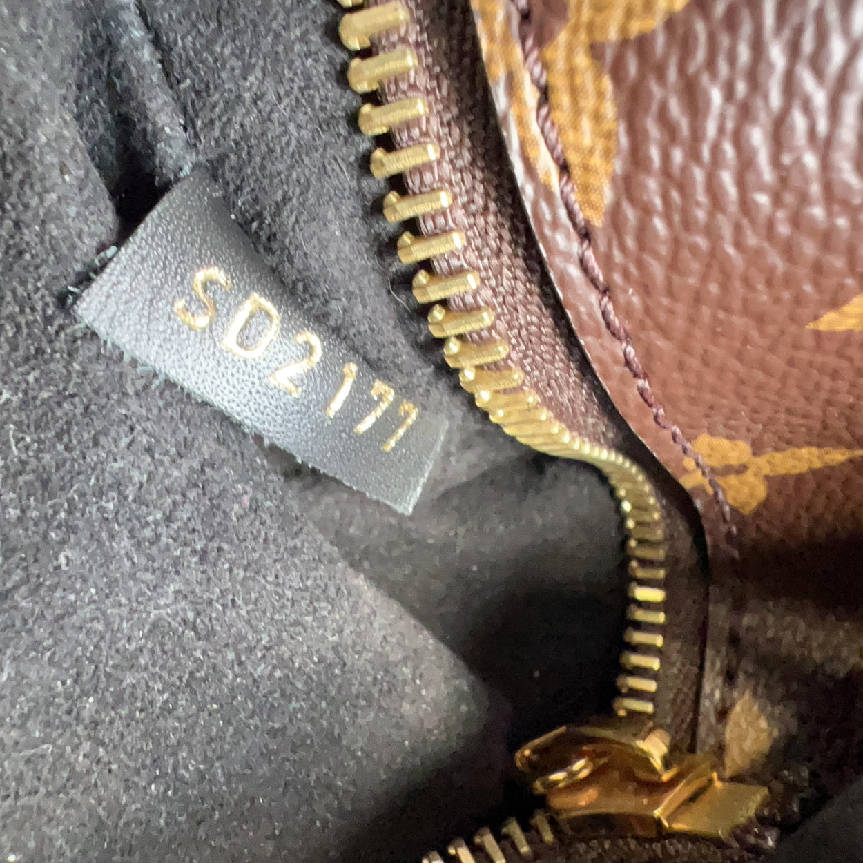 Close-up of a brown textured bag with gold zipper and visible serial number tag.