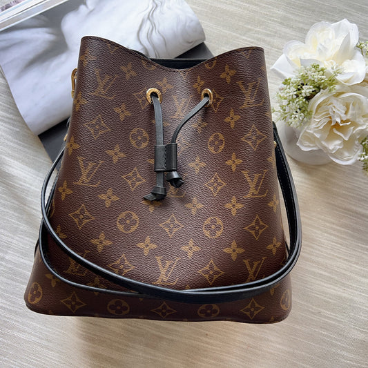 Brown monogram handbag on a light wooden surface with white flowers.