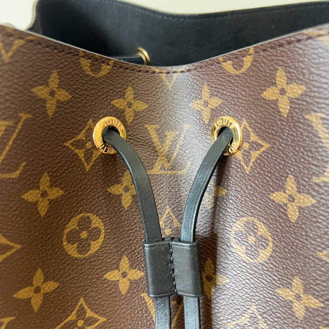 Close-up of a brown handbag with gold monogram pattern and black straps.