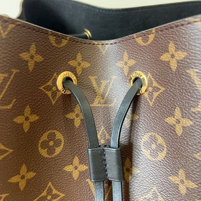 Close-up of a brown handbag with gold monogram pattern and black straps.