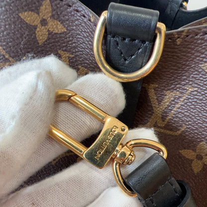 Close-up of a gold and black handbag strap with a brand logo on a patterned background.