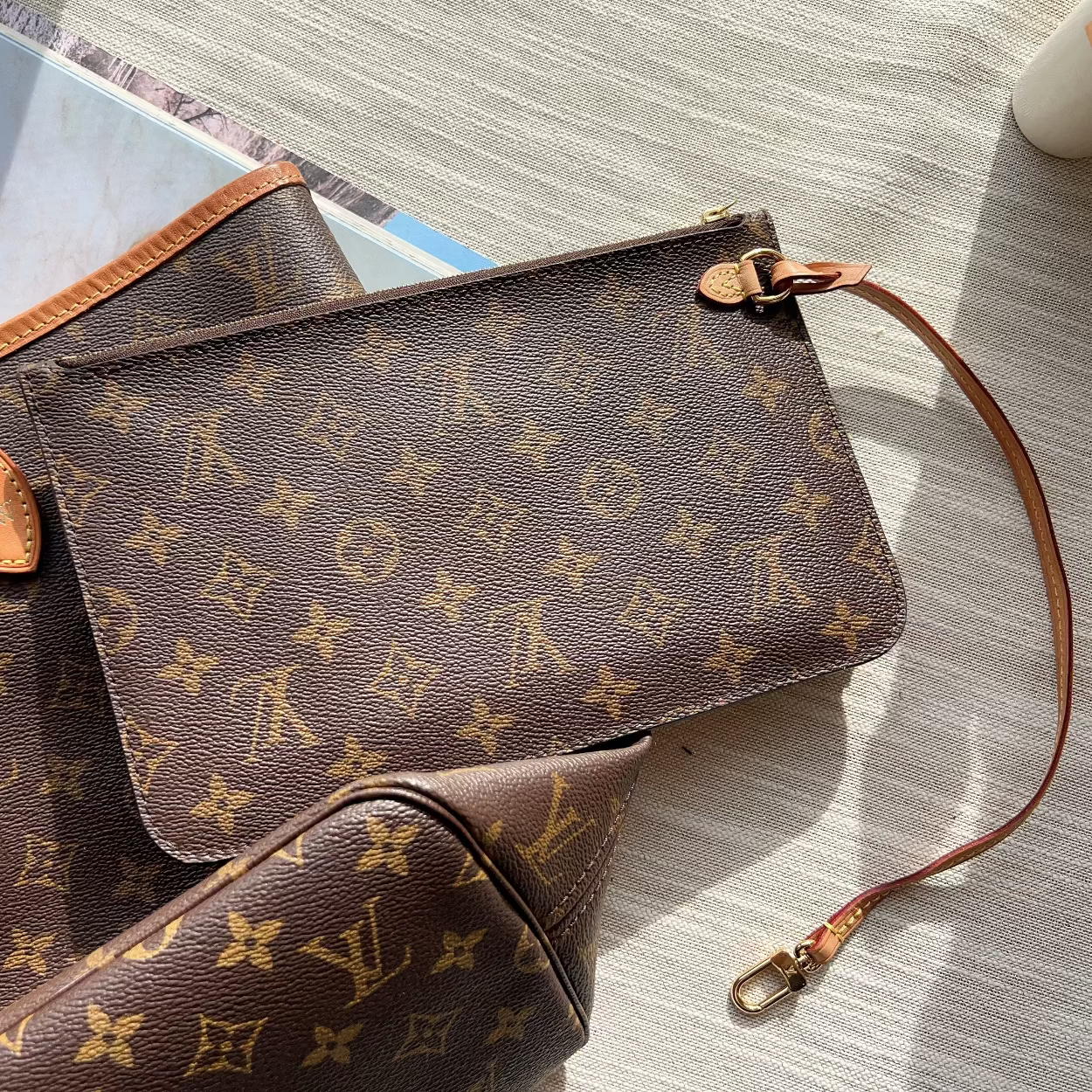 Louis Vuitton monogram canvas shoulder bag in brown with tan leather trim, shown with matching pouches on a light wood surface.