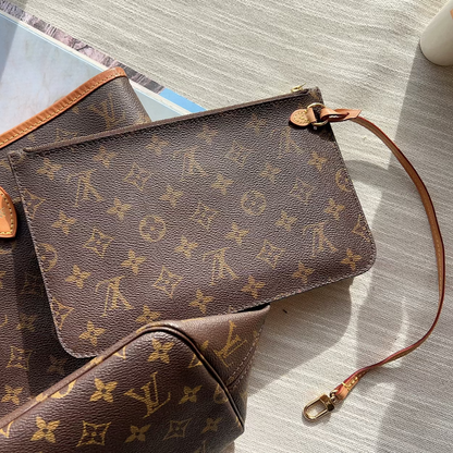 Louis Vuitton monogram canvas shoulder bag in brown with tan leather trim, shown with matching pouches on a light wood surface.