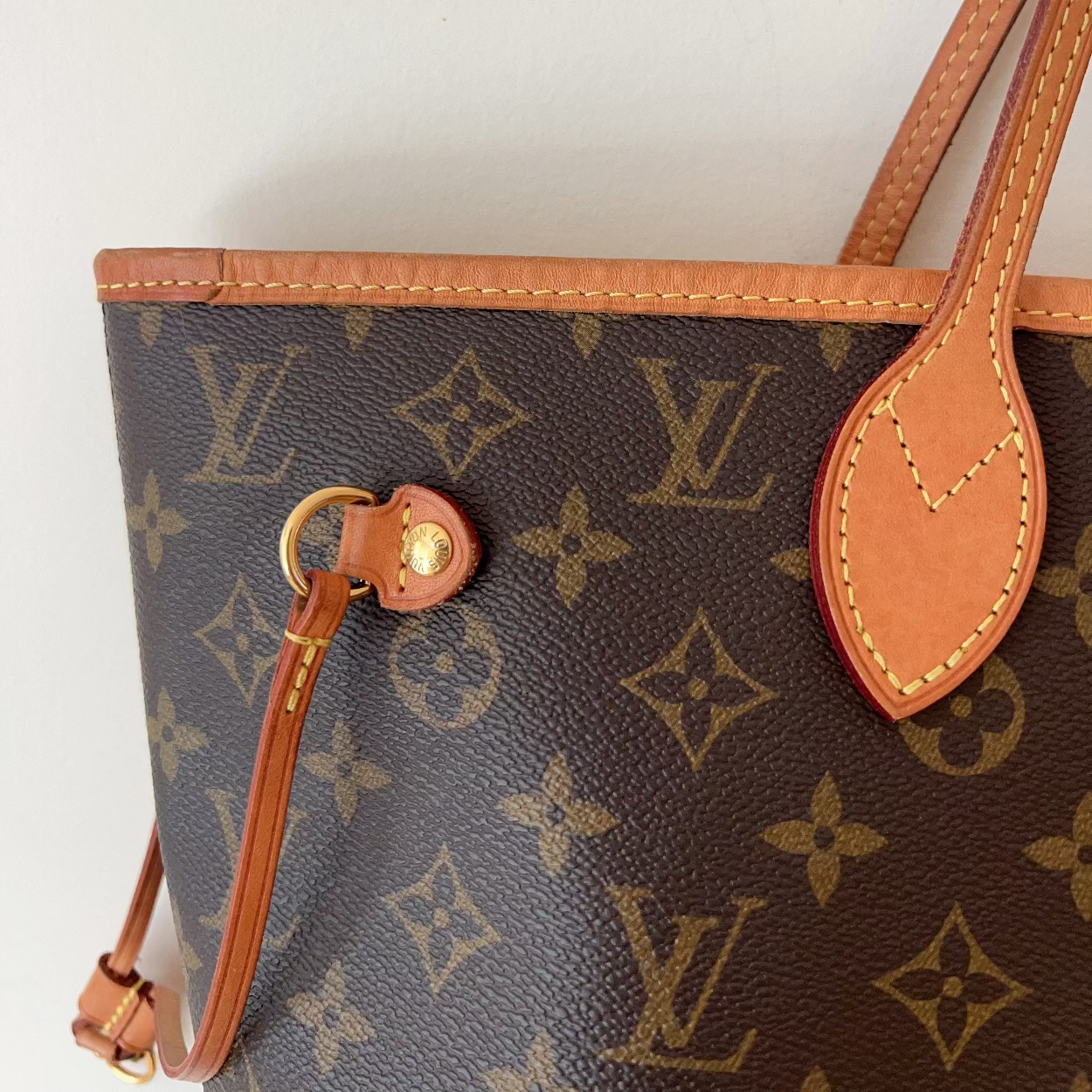 Close-up of a Louis Vuitton monogram tote bag in brown coated canvas with tan leather trim and handles, shown against a plain light background.