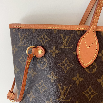 Close-up of a Louis Vuitton monogram tote bag in brown coated canvas with tan leather trim and handles, shown against a plain light background.