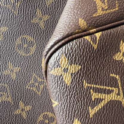 Close-up of brown textured leather with a gold Louis Vuitton monogram pattern, showing part of a bag or cushion seam.