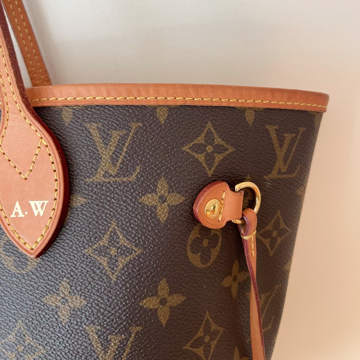 Close-up of a Louis Vuitton monogram canvas handbag in dark brown with tan leather trim and strap, featuring gold-tone hardware and a monogram pattern.