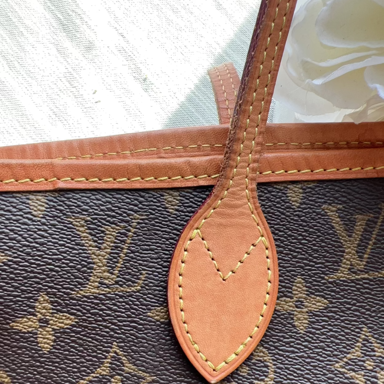 Close-up of a Louis Vuitton monogram bag in dark brown coated canvas with tan leather trim and a matching leather tab, photographed against a light fabric background.