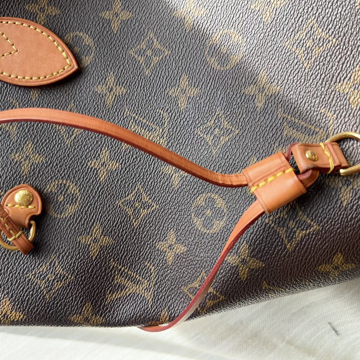 Close-up of a brown Louis Vuitton monogram canvas bag with tan leather strap and gold-tone hardware, laid on a white surface.