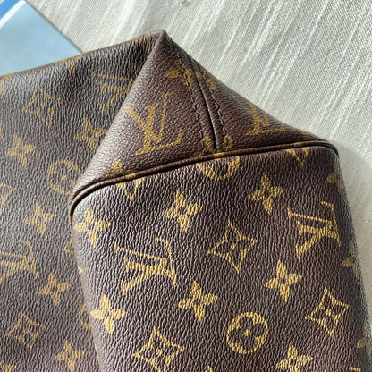 Close-up of a Louis Vuitton monogram canvas bag in dark brown with gold print, showing the classic LV logo pattern and leather trim.