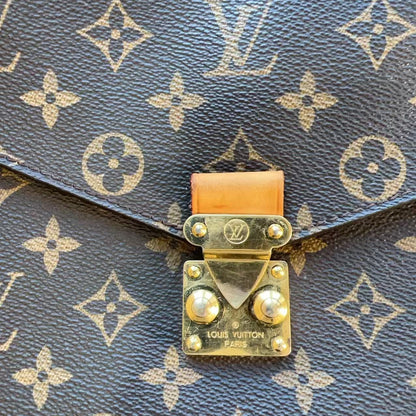 Close-up of a Louis Vuitton monogram canvas bag with a gold-tone metal clasp and a small piece of natural vachetta leather.