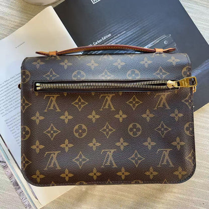 A Louis Vuitton monogram canvas zippered pouch or organizer, shown from above on top of books and a magazine. The brown coated canvas features the classic tan/gold LV monogram pattern, with a gold-tone zipper and a brown leather wristlet strap.