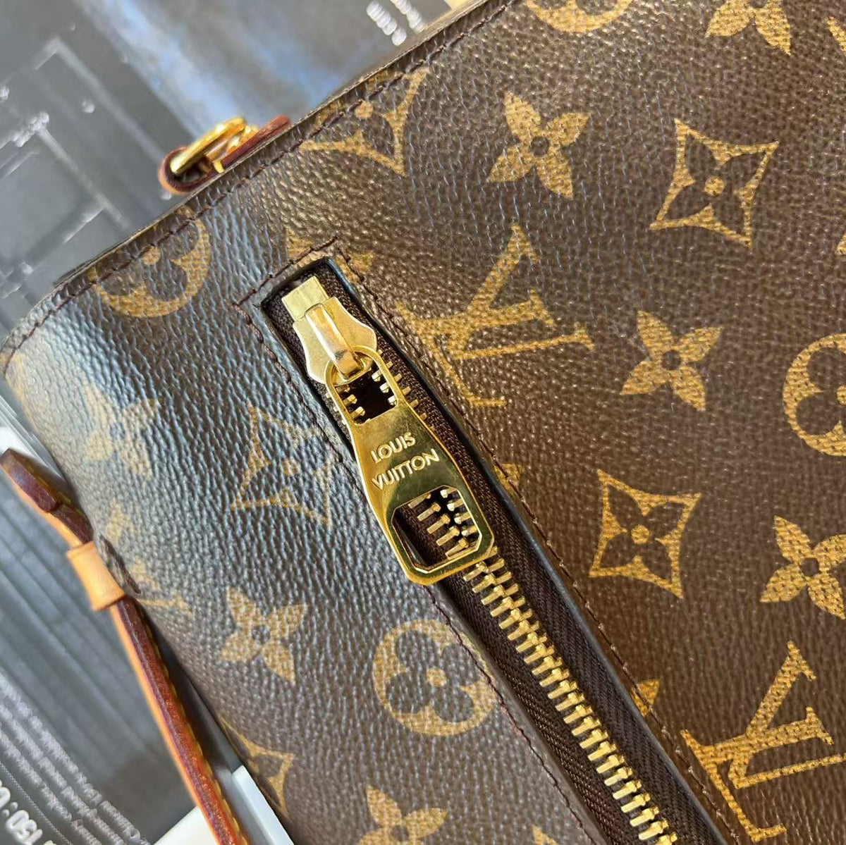 Close-up of a Louis Vuitton monogram canvas pouch or wallet with a gold-tone zipper and a visible Louis Vuitton zipper pull, set against a dark textured background.