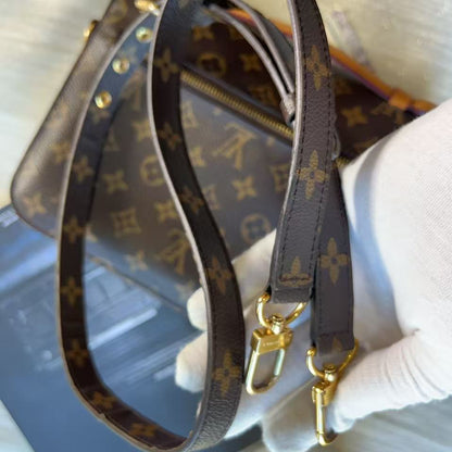 A Louis Vuitton monogram shoulder bag with a detachable brown monogram canvas strap, held by a hand wearing a white glove. The bag features gold-tone hardware and the classic LV monogram pattern.