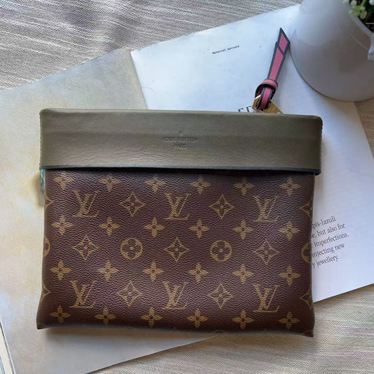 A Louis Vuitton monogram pouch with a dark olive green leather flap, resting on white papers with a small white pot in the background.
