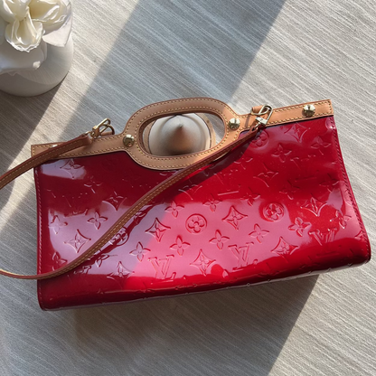 Red handbag with brown strap on a light gray surface