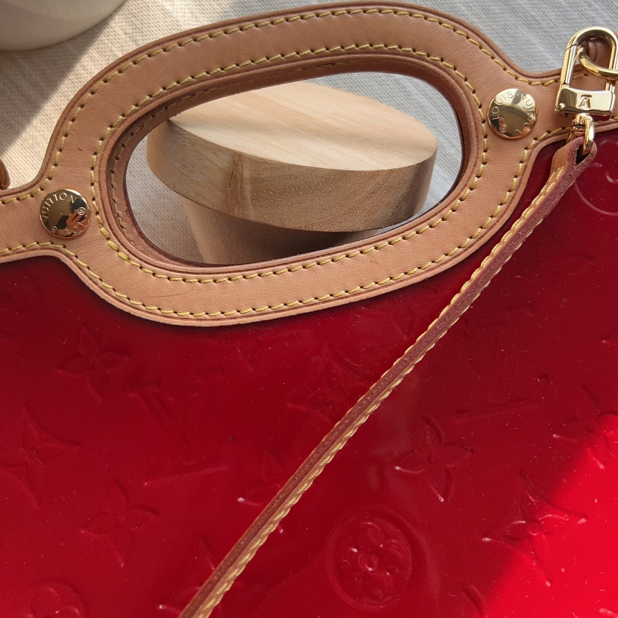 Red handbag with gold handle and strap on a textured surface