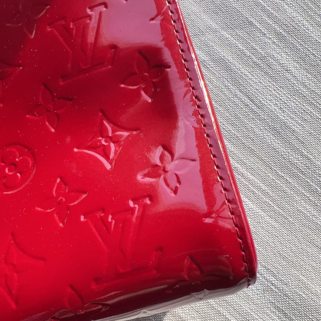 Red patent leather wallet with embossed logo on a light gray surface